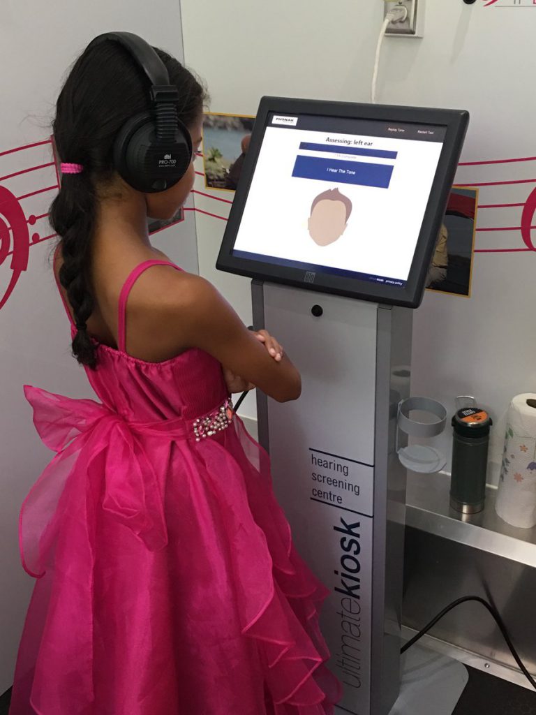 A young girl testing her hearing at an Ultimate Kiosk